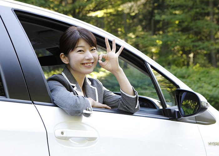 運転席から顔を出して親指と人差し指でOKの形を作っている女性