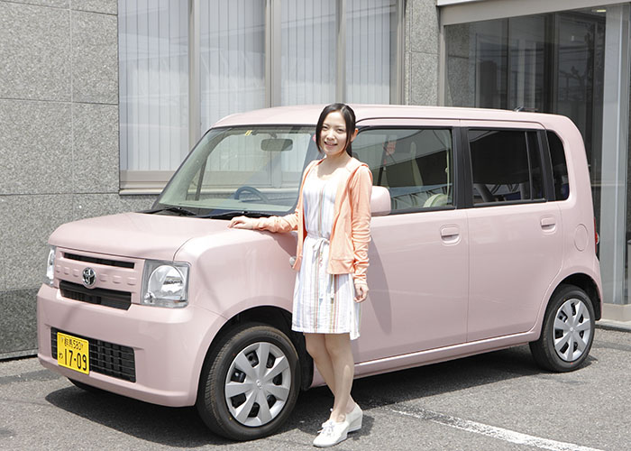 淡いピンク色の車に手をかけて立っている女性